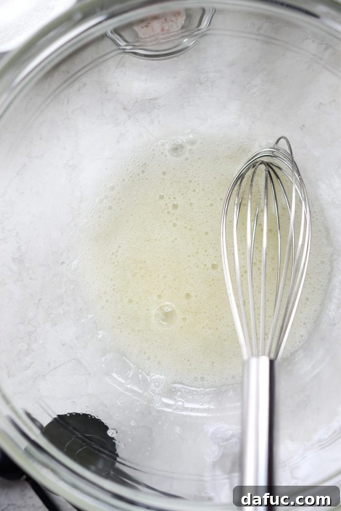 A glass bowl with frothy whisked egg whites, ready for coating pecans