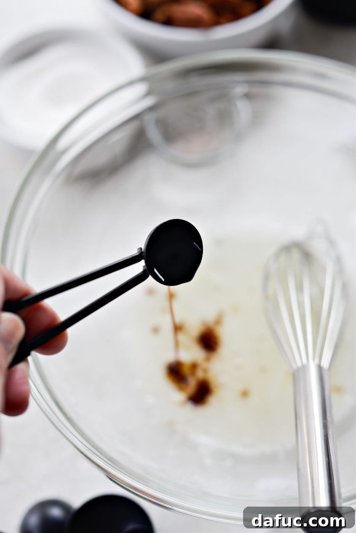 A hand adding vanilla extract to whisked frothy egg whites in a bowl