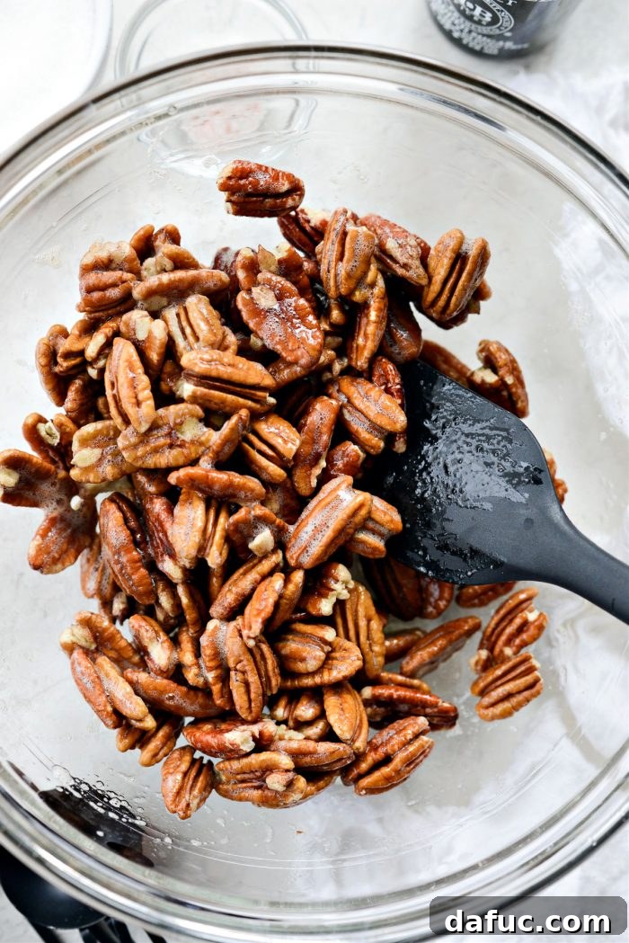 Pecan halves being tossed thoroughly in a bowl with the vanilla egg white mixture
