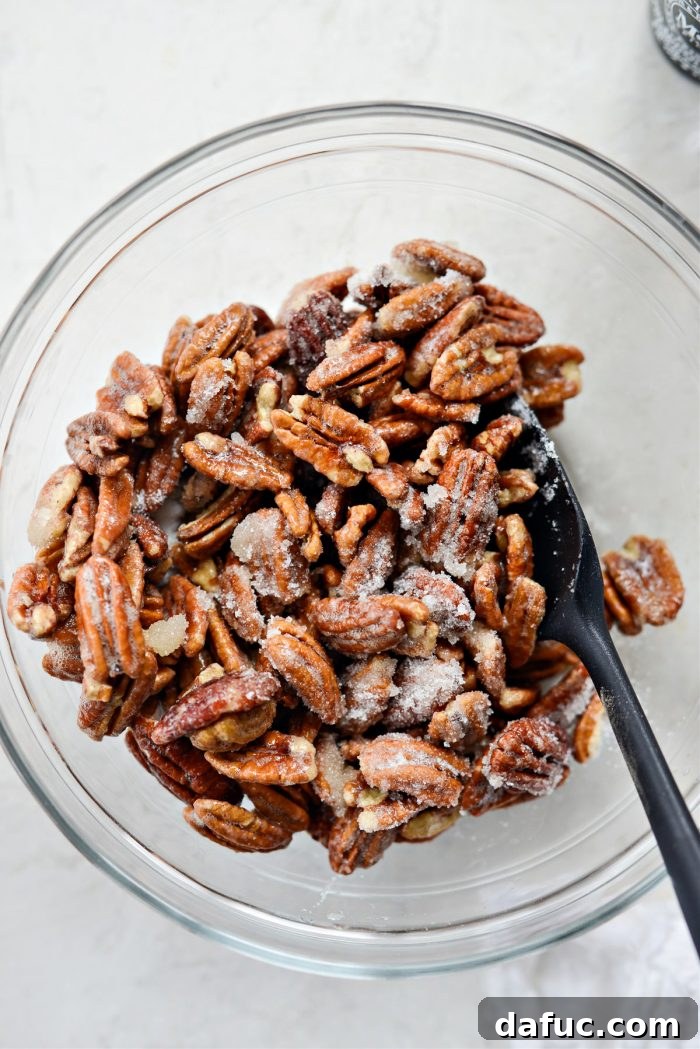 Egg white-coated pecans being transferred to a bowl of sugar and tossed to coat completely