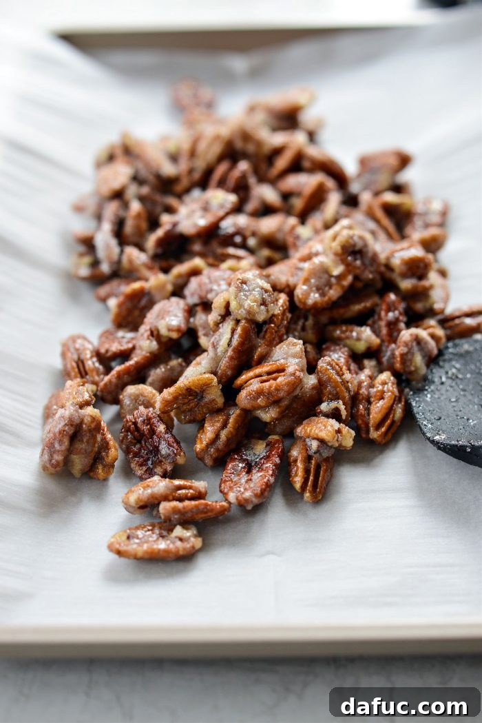 The sugar-coated pecan mixture spread out in a single layer on a parchment-lined rimmed baking sheet