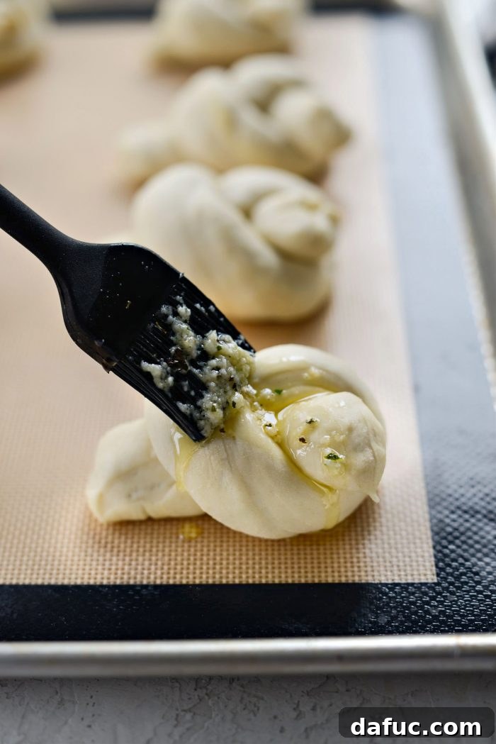 Brushing the garlic herb butter mixture onto the unbaked dough knots