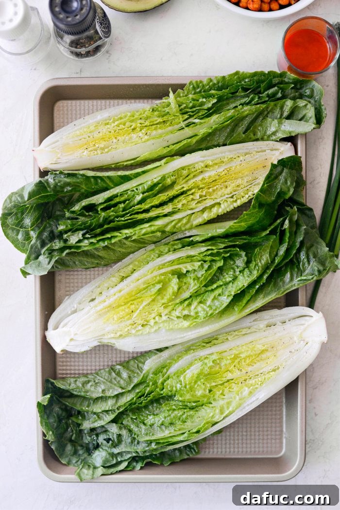 Romaine lettuce halves sprayed with olive oil and seasoned with salt and pepper, ready for air frying.