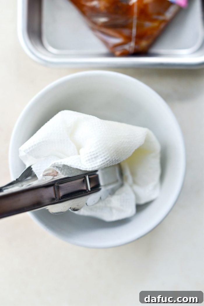 Oiling the hot grill grates with a paper towel dipped in olive oil, held by tongs