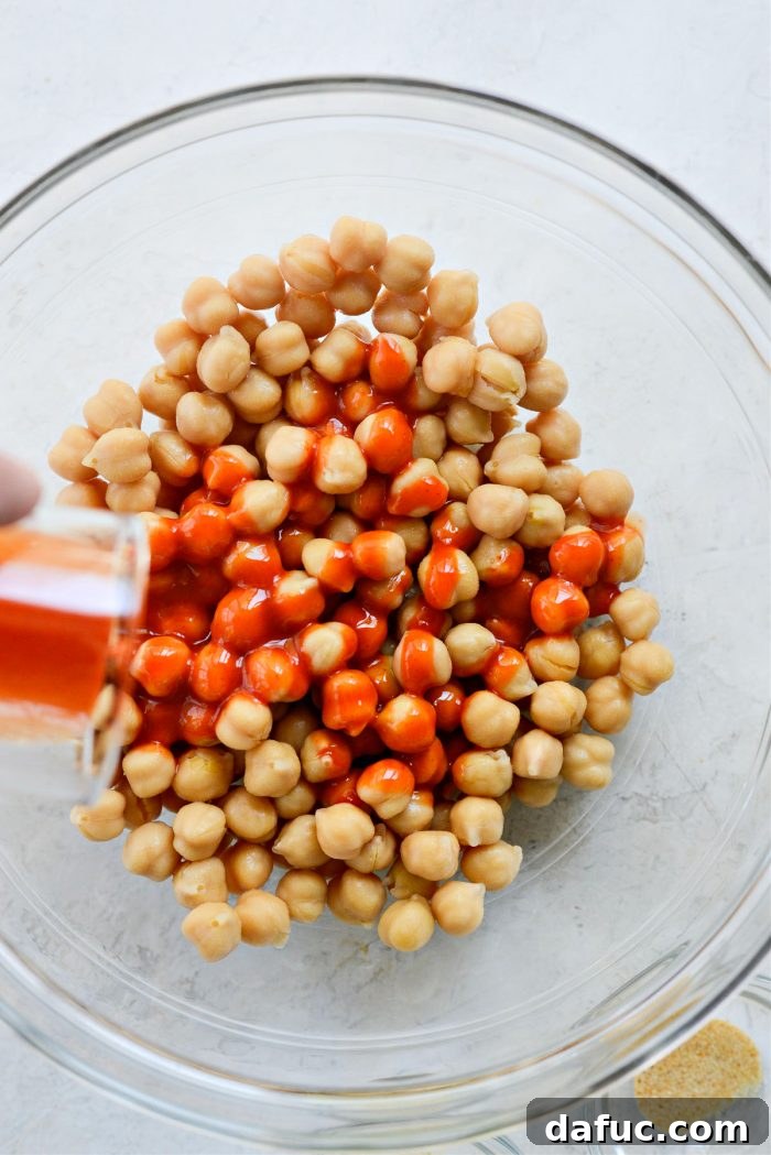 Pouring buffalo sauce over drained chickpeas in a bowl