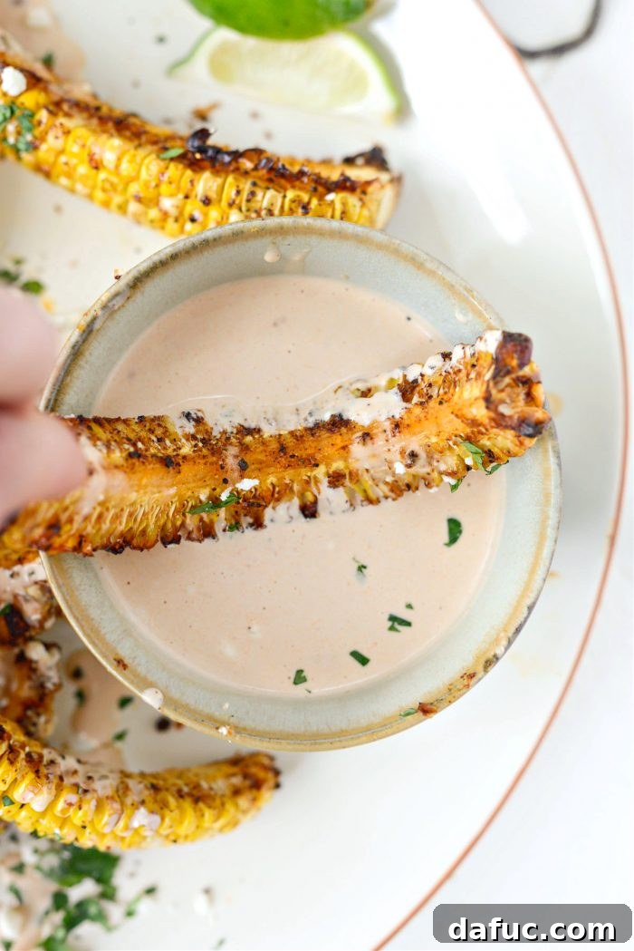 Hand holding an Air Fryer Corn Rib, dipping it into adobo crema