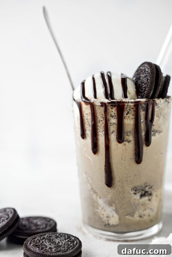 Espresso Cookies and Cream Milkshake 2 Tall glass of Espresso Cookies and Cream Milkshake topped with whipped cream and chocolate cookie crumbles, on a light background.