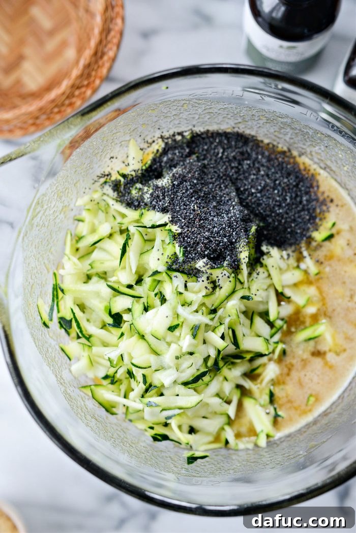 Grated zucchini and poppy seeds being added to the wet ingredient mixture