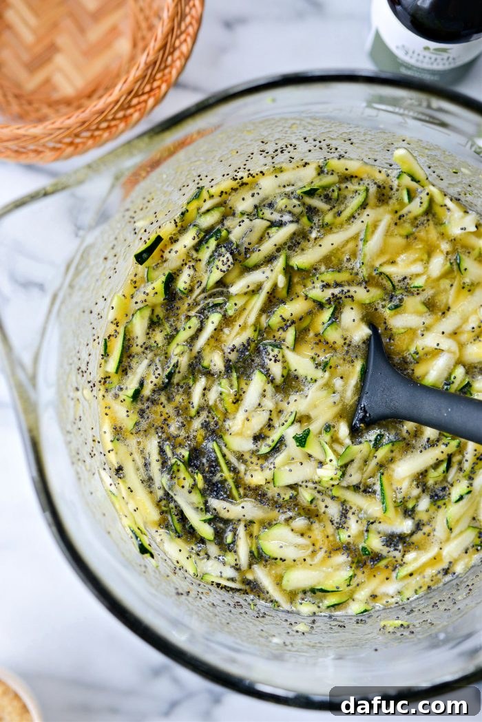 Mixing grated zucchini and poppy seeds into the wet batter with a rubber spatula