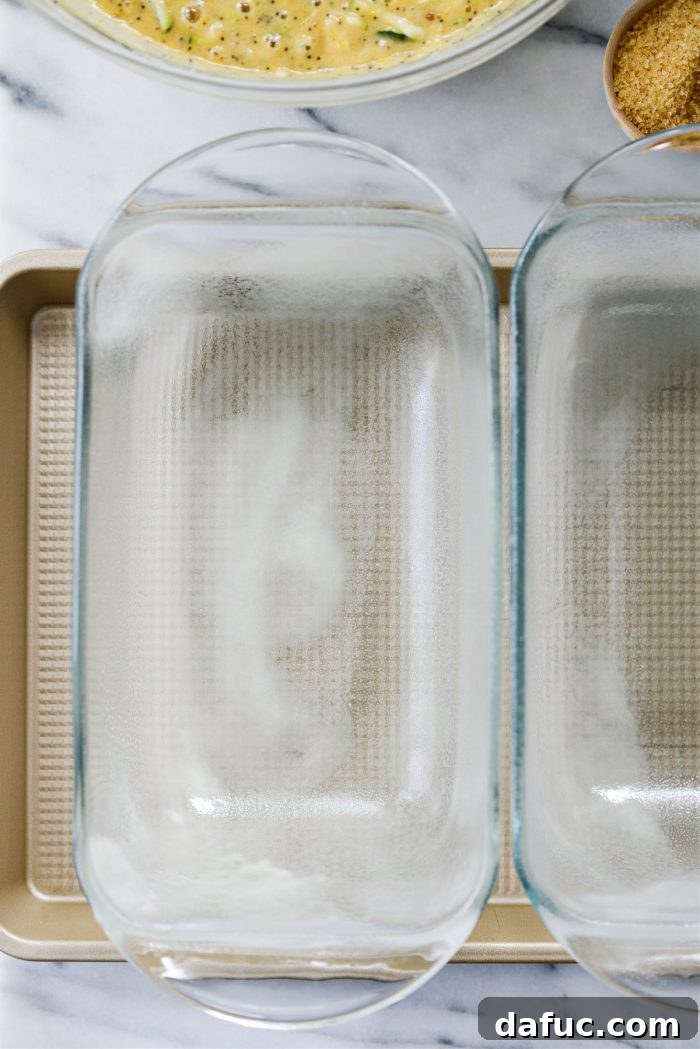 Two metal loaf pans being greased and floured, ready for baking