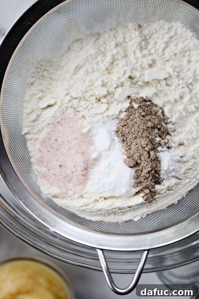 Sifting unbleached flour, baking soda, baking powder, and cardamom into a mesh sieve over a bowl