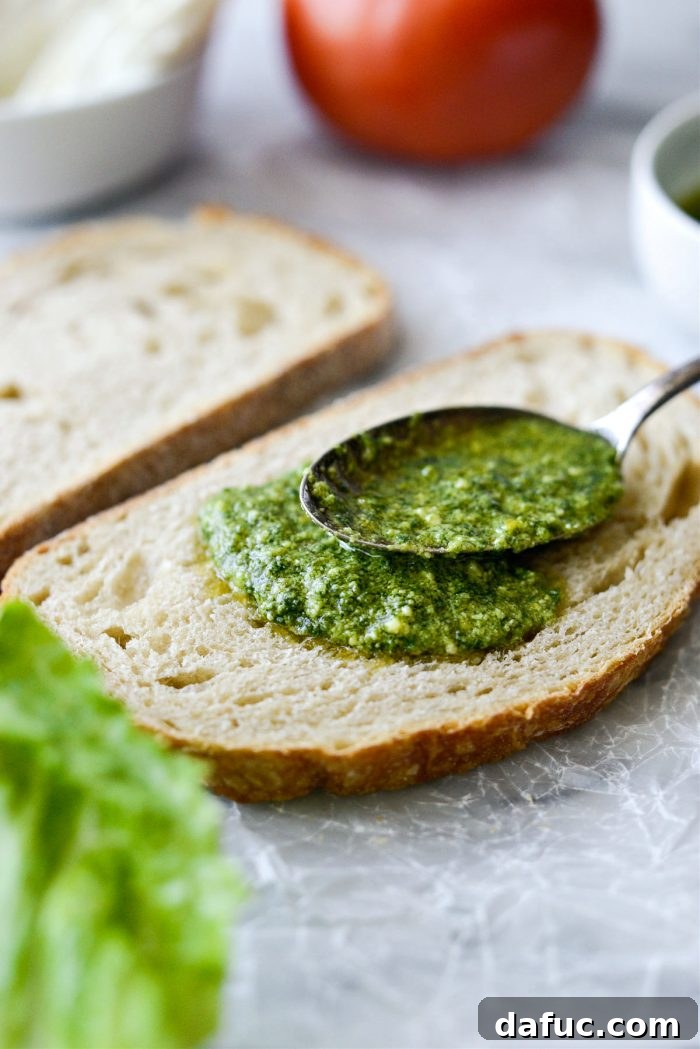 Spreading basil pesto on one side of toasted sourdough bread