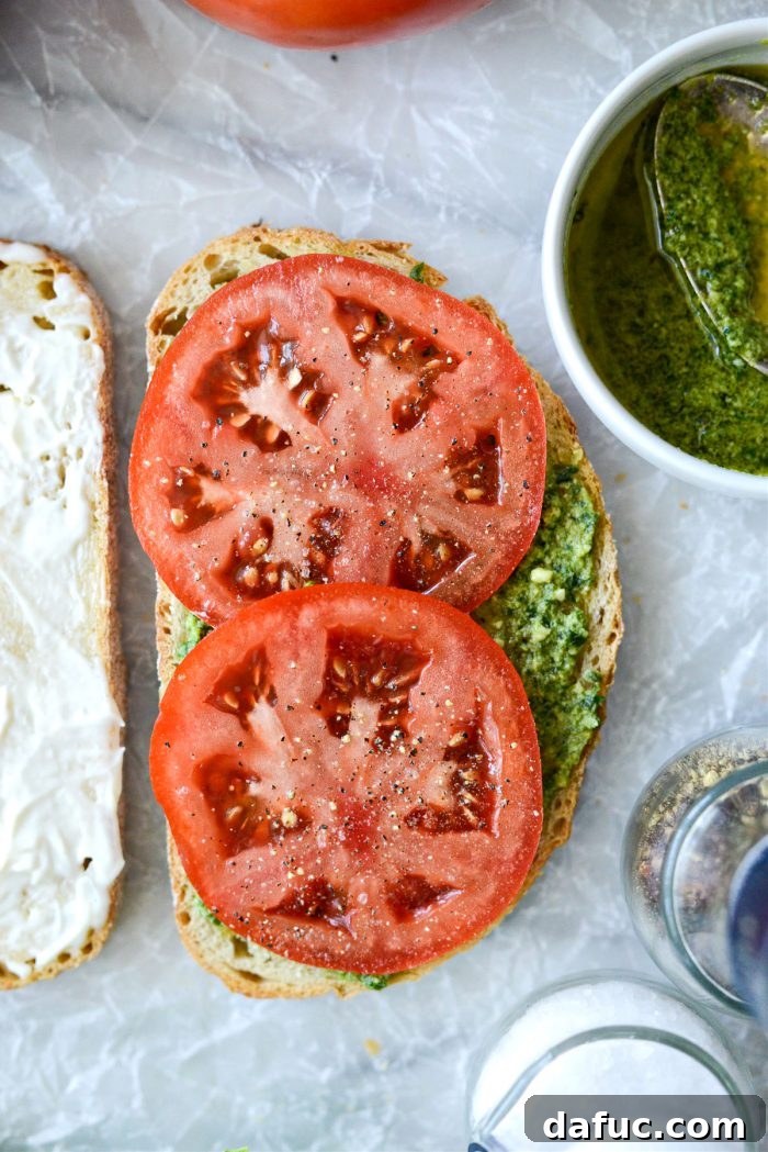 Topping the pesto side with sliced tomato, salt, and pepper