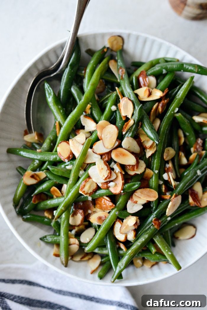 cream bowl of garlicky green beans almondine with spoons.