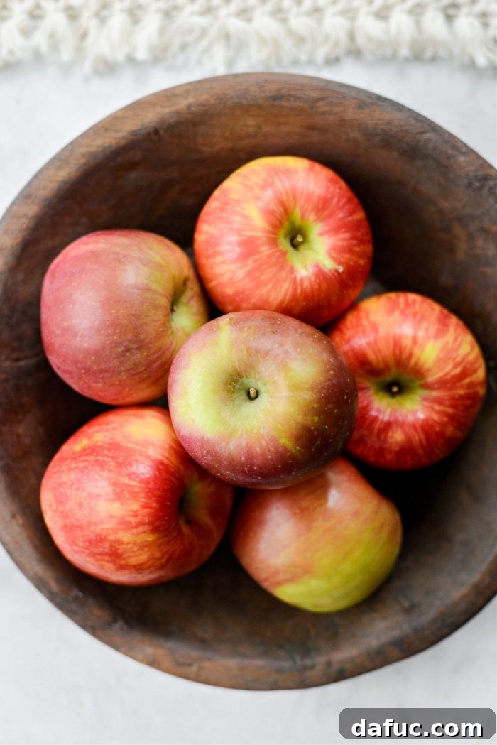 A decorative wooden bowl filled with various types of whole apples, showcasing their natural beauty