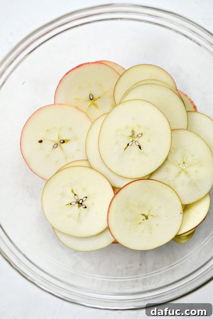 Thinly sliced apples, some coated with lemon juice, resting in a clear glass bowl