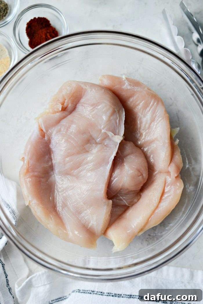 Adding pounded chicken breasts to a bowl for seasoning.