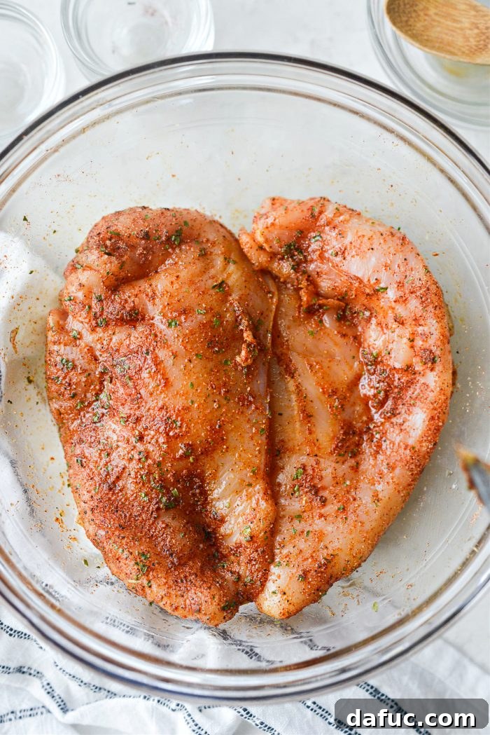 Tossing chicken breasts in oil and seasoning for even coating.