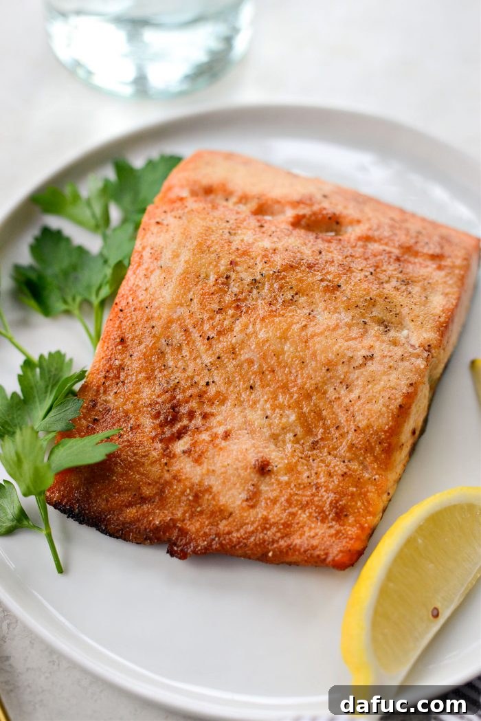 Easy Air Fryer Salmon 11 Air fried salmon served on a plate with fresh lemon wedges and herbs.