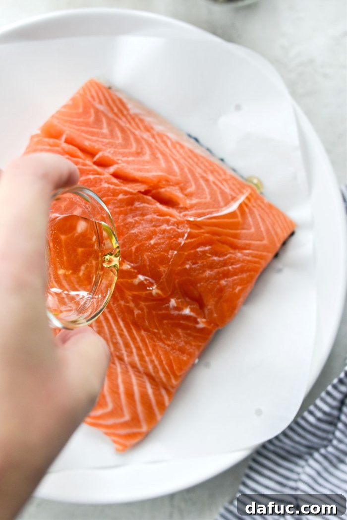 Easy Air Fryer Salmon 4 Avocado oil being drizzled over a salmon filet on parchment paper.