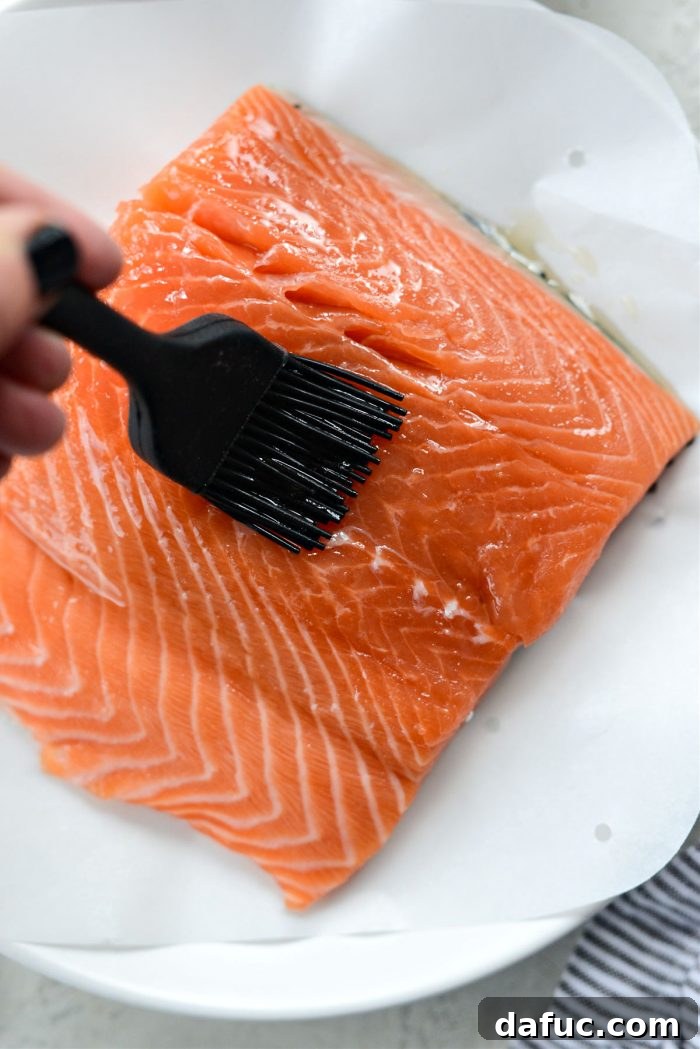 Easy Air Fryer Salmon 5 A hand brushing oil onto the top and sides of a salmon filet.