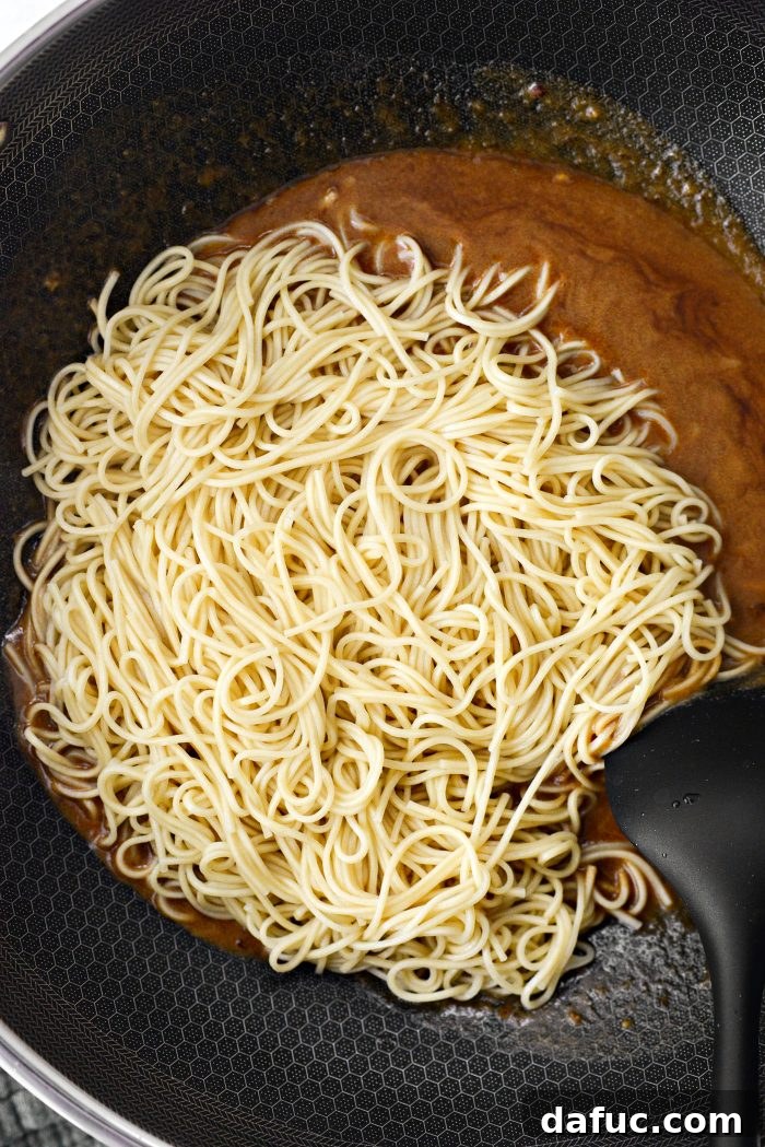Fiery Garlic Sesame Noodles 14 Cooked lo mein noodles being added directly into the simmering spicy garlic sesame sauce in a large wok.