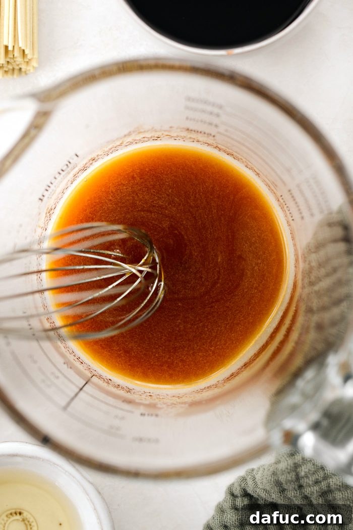 Fiery Garlic Sesame Noodles 8 A hand whisking the mixture of brown sugar, bouillon, and hot water in a measuring cup until fully dissolved.