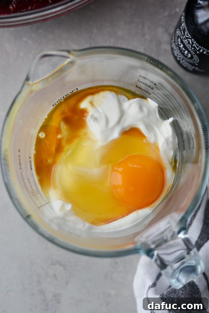 Crimson Kitchen 13 Ingredients for the sour cream topping: sour cream, an egg, and vanilla extract in a liquid measuring cup.