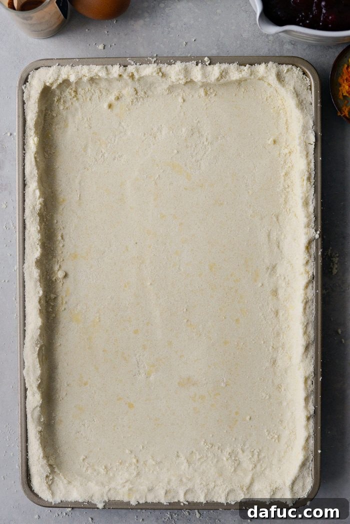 Crimson Kitchen 9 The cake mixture pressed into the pan, showing a slightly raised edge around the sides, ready for partial baking.