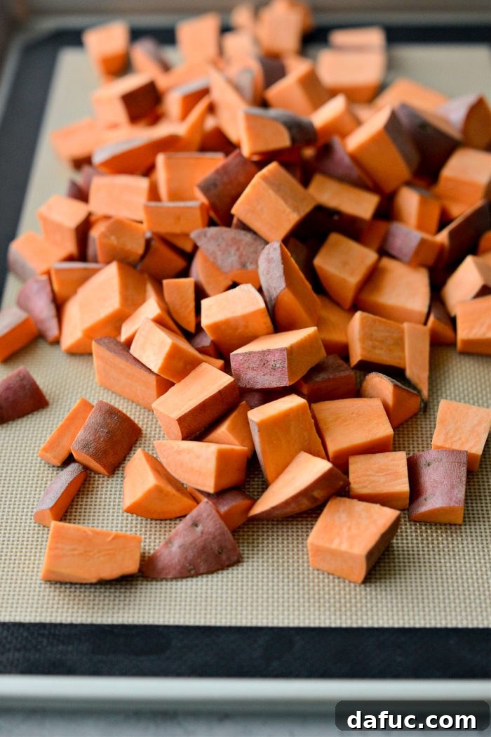 Diced sweet potatoes evenly spread on a parchment-lined baking sheet, ready for seasoning
