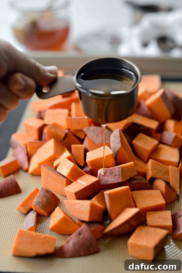 Diced sweet potatoes being generously drizzled with olive oil on a baking pan