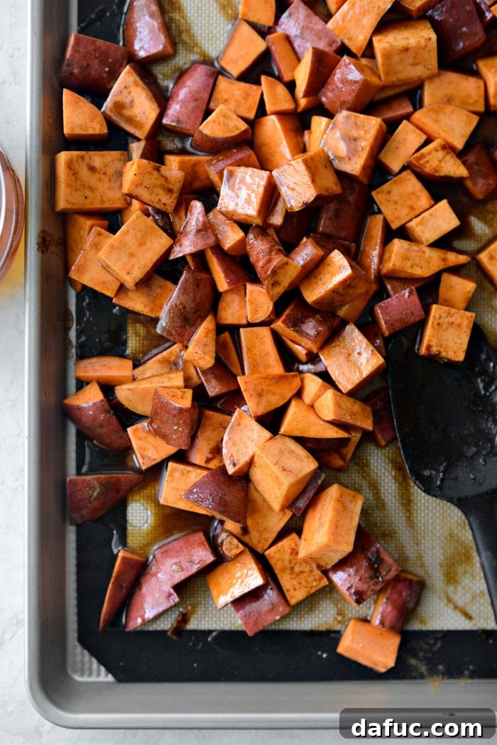 Sweet potatoes being tossed thoroughly with a spatula to evenly coat them in the glaze