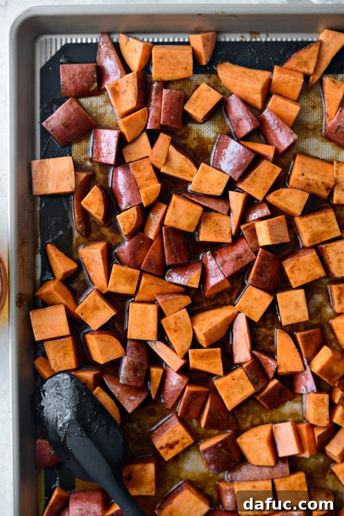 Seasoned sweet potatoes spread out in a single layer on a baking sheet, ready for the oven