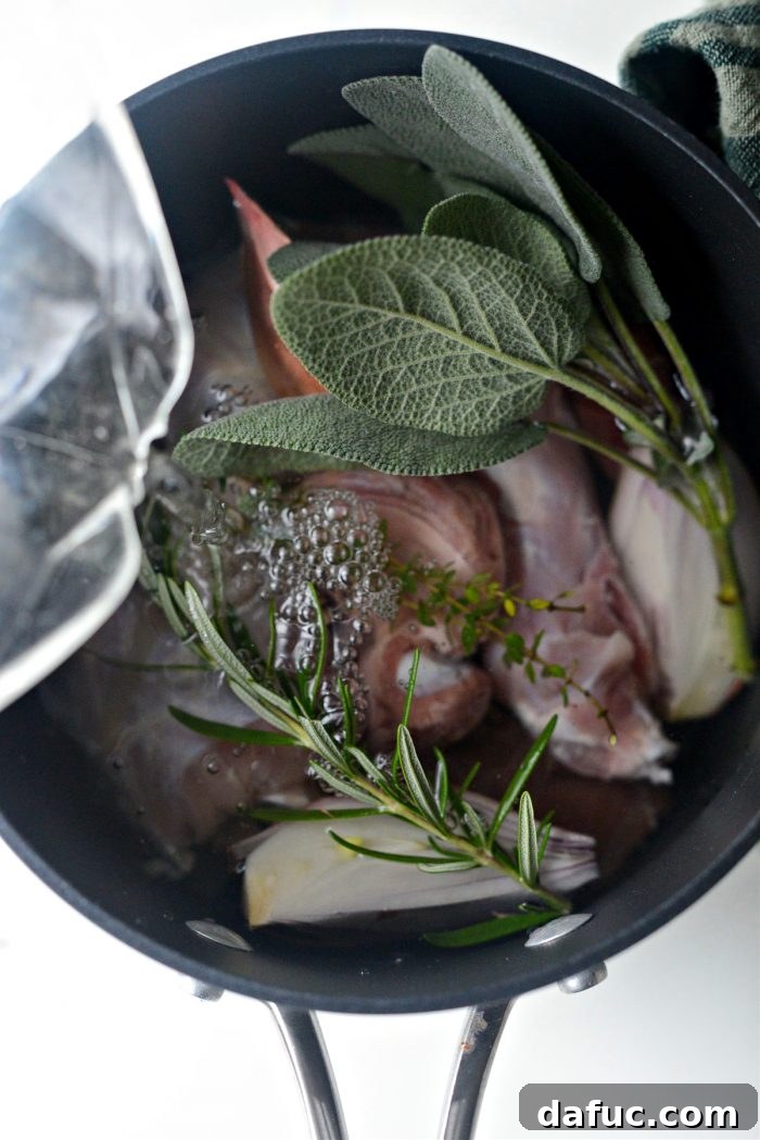 Turkey neck and giblets simmering with fresh herbs and shallot in a saucepan