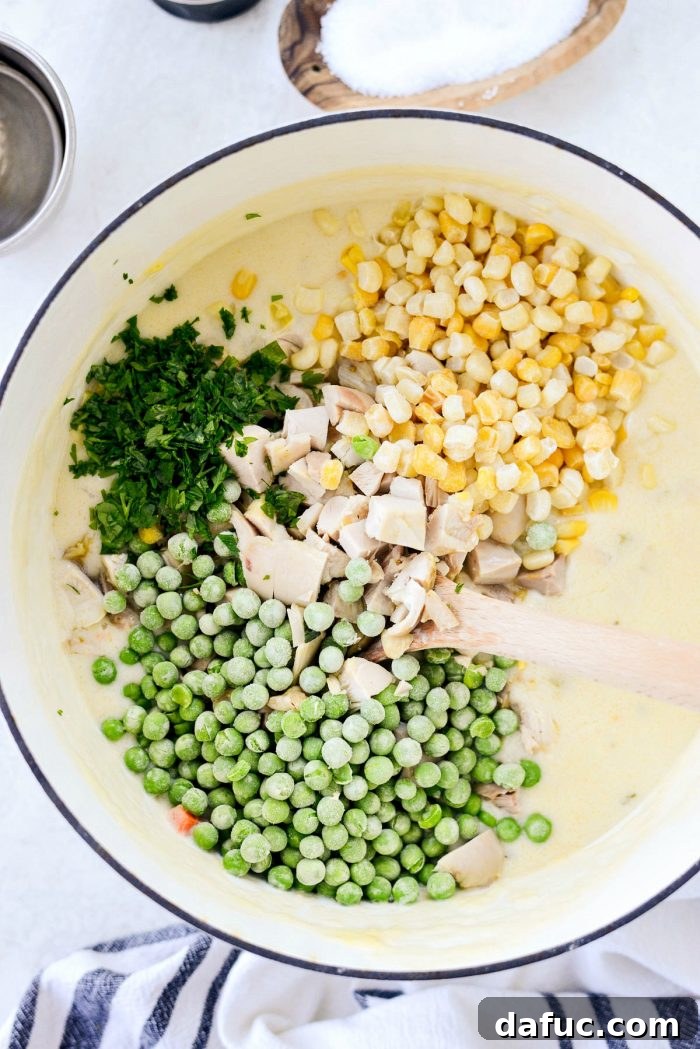 Thickened pot pie filling removed from heat, with cooked chicken, frozen peas, corn, and fresh parsley added.