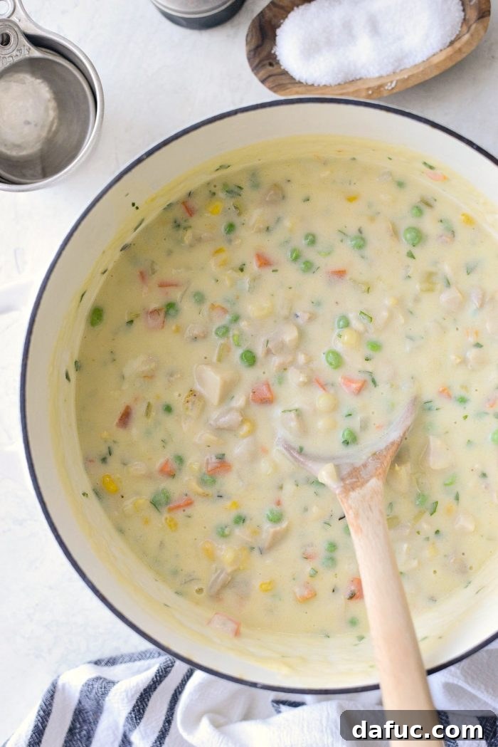 Pot pie filling being stirred and seasoned with salt and black pepper.