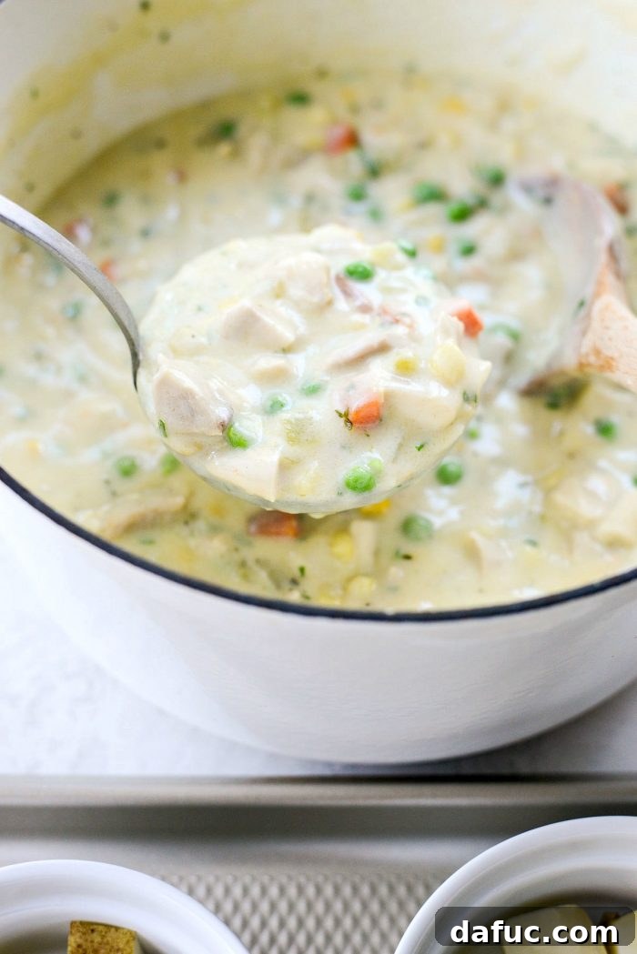 Creamy chicken pot pie filling being ladled over potatoes in ramekins.