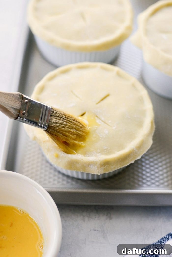 Egg wash being brushed onto the pie crust tops of individual chicken pot pies.