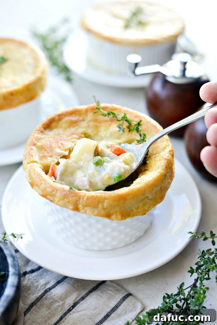 Close-up of a single homemade chicken pot pie, showing the flaky crust and creamy filling, with a fork ready to dig in.