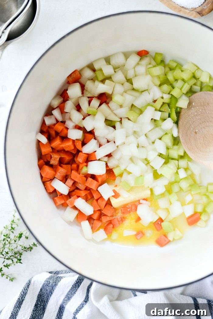 Diced carrots, celery, and onion being added to melted butter in a pot.