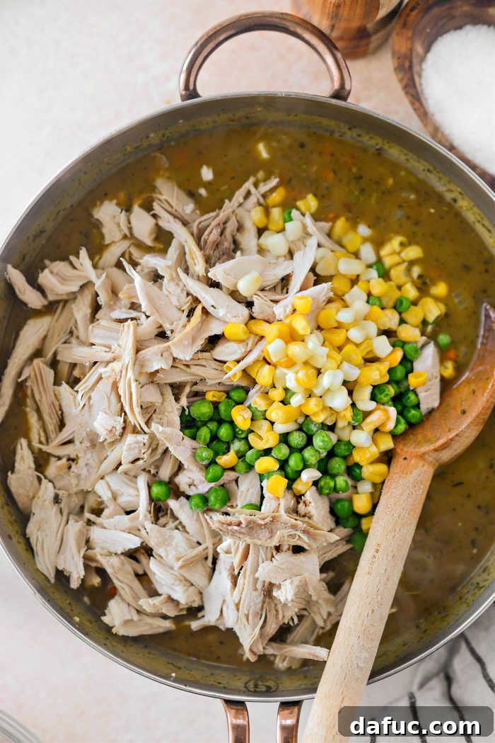 Adding shredded leftover turkey, frozen peas, and corn to the gravy-based filling