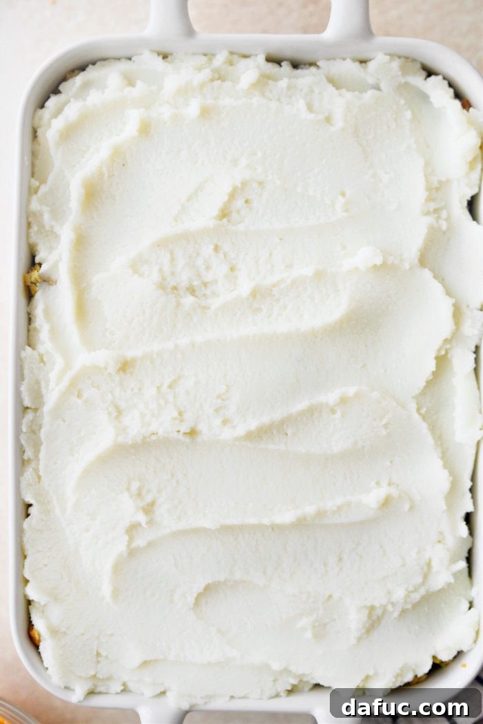 Spreading smooth mashed potatoes evenly over the stuffing layer for the casserole topping