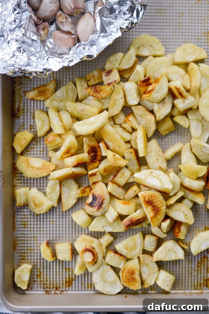 Golden Roasted Parsnip Puree 13 Close-up of roasted parsnips and garlic on a baking sheet, showing caramelization.