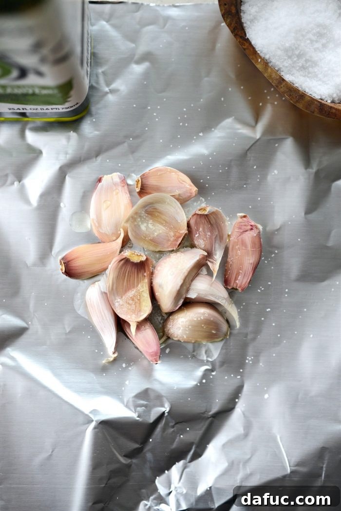 Golden Roasted Parsnip Puree 8 Garlic cloves on aluminum foil, drizzled with olive oil and seasoned with salt, ready to be formed into a pouch.