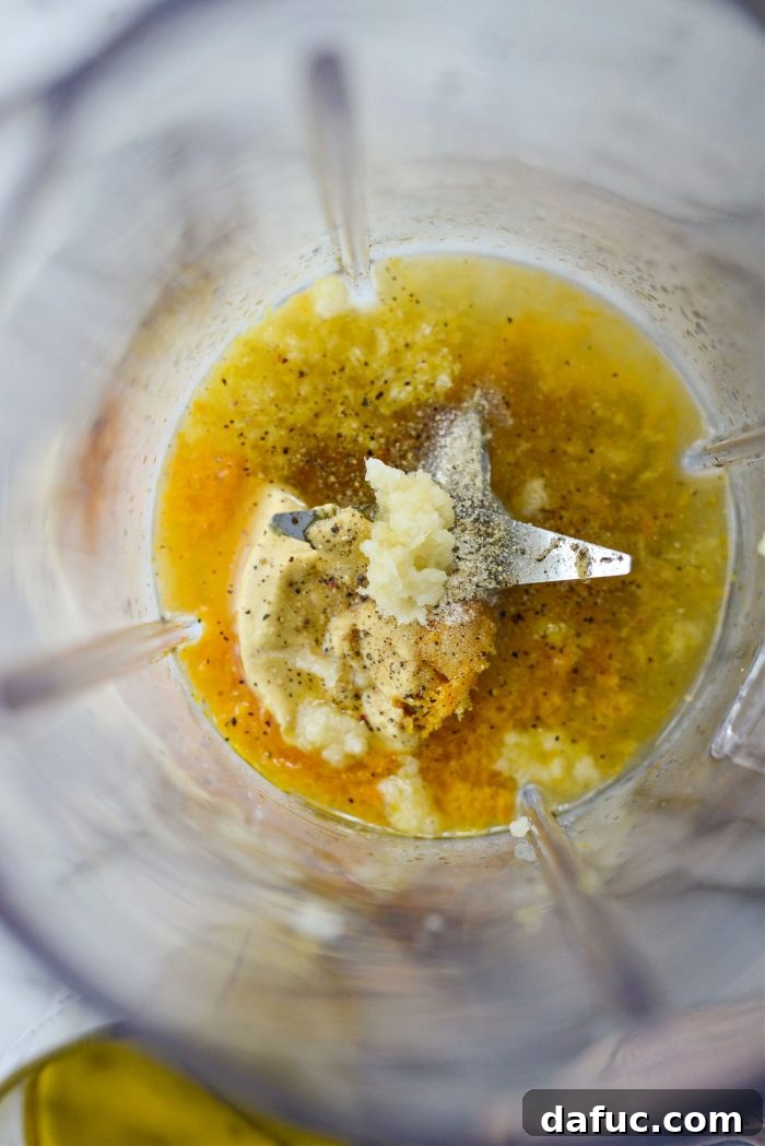 Adding dijon, onion powder, black pepper, and grated fresh garlic to blender