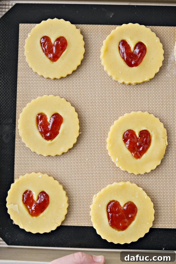 Jam Filled Butter Heart Cookies 15 Jam Heart Butter Cookies baking on a baking sheet in the oven, with edges just starting to turn golden.