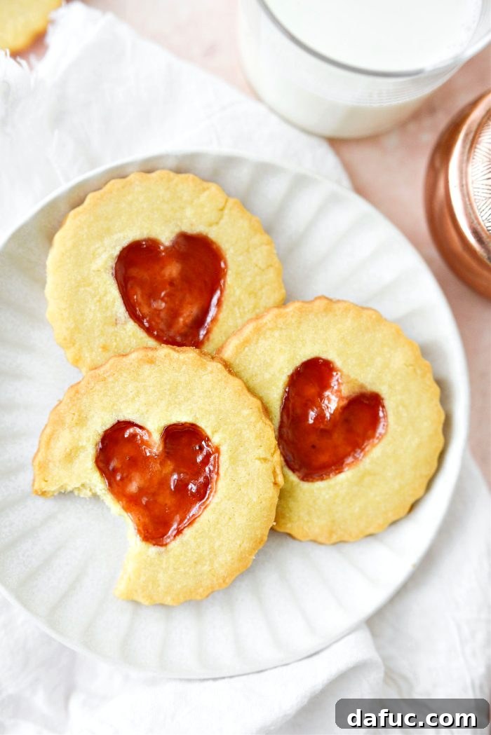 Jam Filled Butter Heart Cookies 3 Close-up of a stack of freshly baked Jam Heart Butter Cookies, highlighting the glistening, bright red jam-filled centers and golden-brown edges.