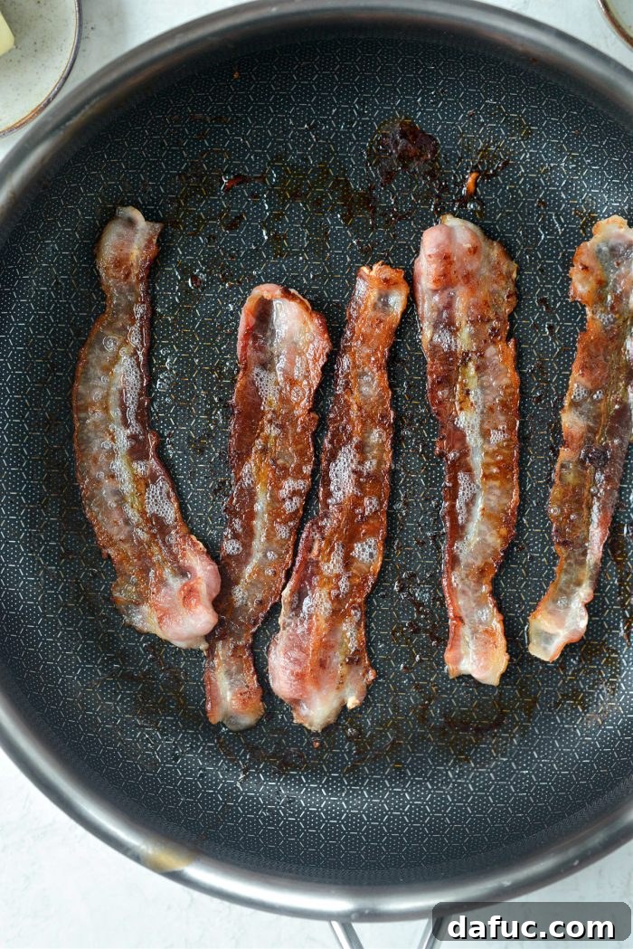 Crispy bacon strips being cooked in a skillet