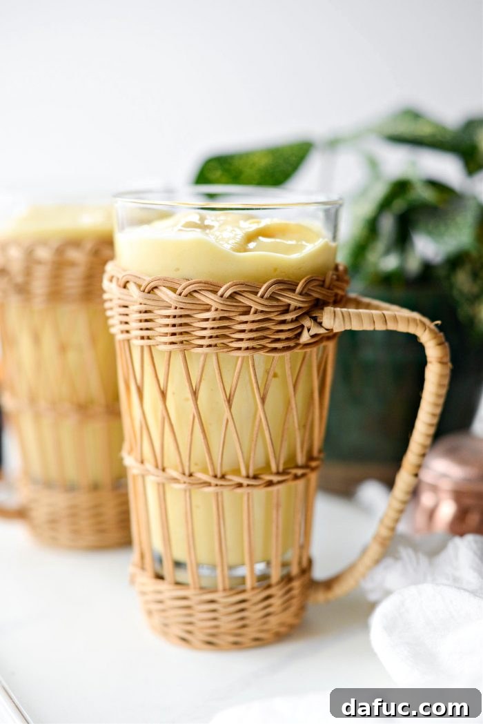 Liquid Sunshine Mango 11 Golden Hour Mango Smoothie poured into two tall glasses, garnished with a mango slice and a straw, ready to be served.