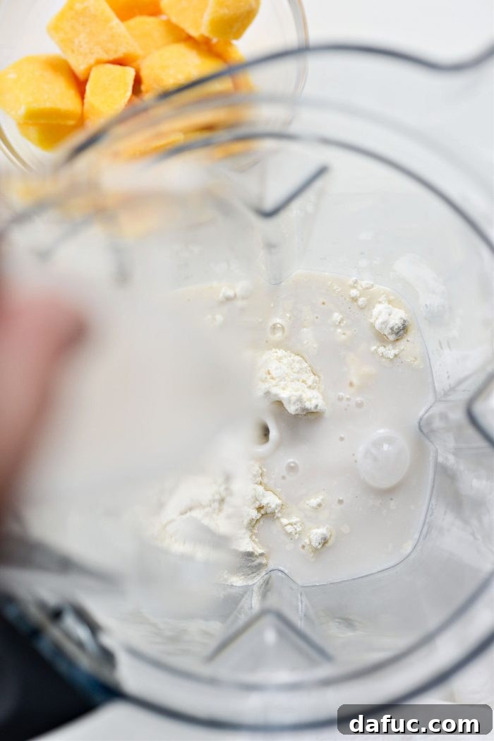 Liquid Sunshine Mango 7 Vanilla protein powder being scooped into a blender, followed by macadamia nut milk being poured in, illustrating the next steps.